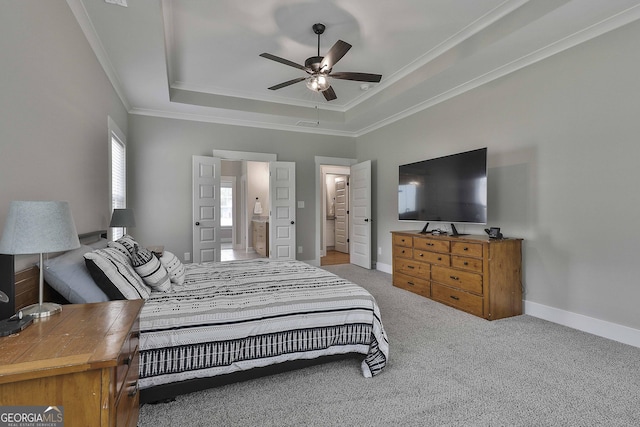 bedroom featuring crown molding, ensuite bath, carpet flooring, ceiling fan, and a tray ceiling