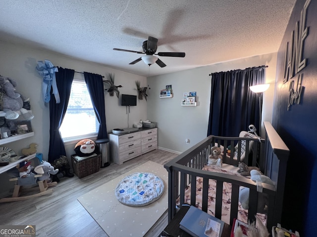 bedroom featuring a crib, a textured ceiling, light wood-type flooring, and ceiling fan