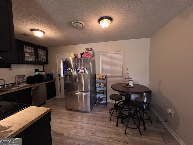 kitchen with appliances with stainless steel finishes, a textured ceiling, light hardwood / wood-style flooring, and sink