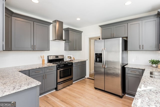 kitchen with wall chimney exhaust hood, gray cabinets, light stone counters, and stainless steel appliances