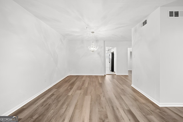 spare room with a chandelier and light wood-type flooring