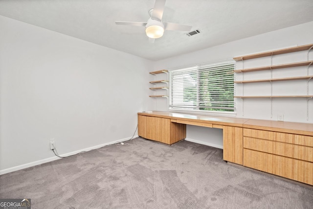 unfurnished office featuring ceiling fan, built in desk, and light carpet