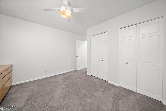 unfurnished bedroom featuring two closets, ceiling fan, and dark colored carpet