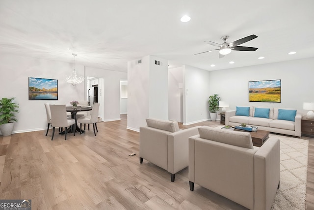 living room with ceiling fan with notable chandelier and light hardwood / wood-style floors