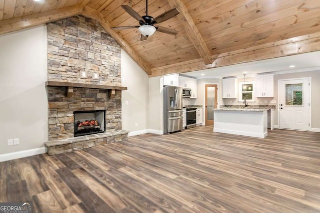 unfurnished living room with hardwood / wood-style floors, lofted ceiling with beams, a stone fireplace, ceiling fan, and wood ceiling