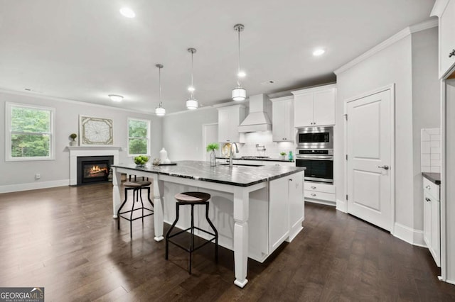 kitchen featuring white cabinetry, premium range hood, appliances with stainless steel finishes, and an island with sink