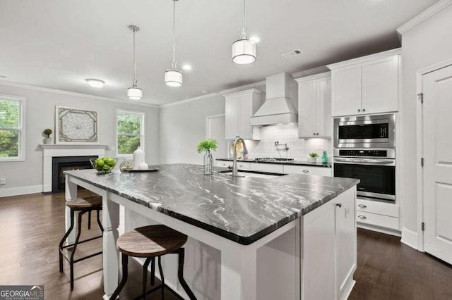 kitchen featuring premium range hood, white cabinetry, a center island with sink, and pendant lighting