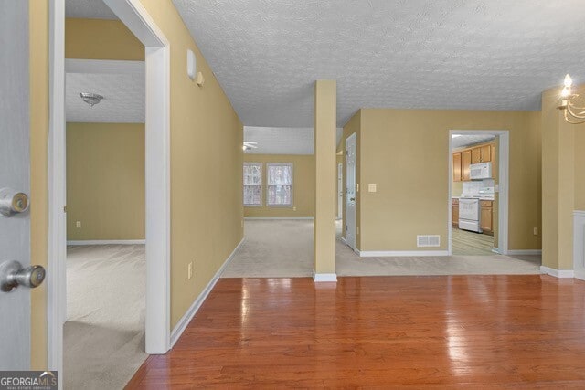 unfurnished room with light hardwood / wood-style flooring, a textured ceiling, and an inviting chandelier