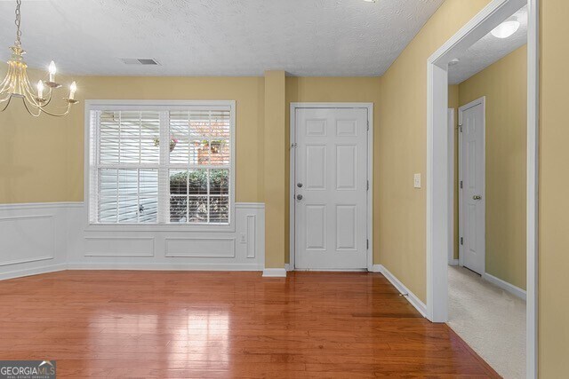 foyer with wood-type flooring, a textured ceiling, and an inviting chandelier