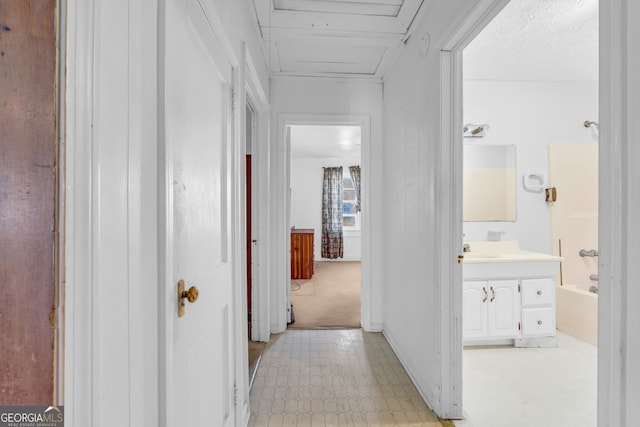 hallway with a textured ceiling, light colored carpet, and sink