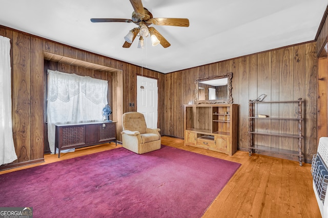 unfurnished room featuring heating unit, light hardwood / wood-style floors, ceiling fan, and wood walls