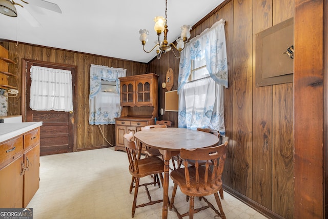 dining space with wooden walls, crown molding, and ceiling fan with notable chandelier