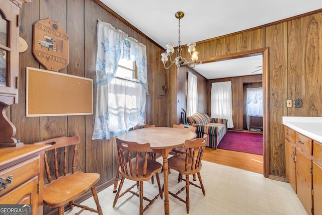 dining room with ornamental molding, wooden walls, and a chandelier