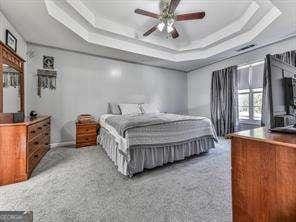 bedroom featuring a raised ceiling, ceiling fan, and carpet