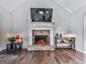 living room with hardwood / wood-style flooring, a stone fireplace, and lofted ceiling