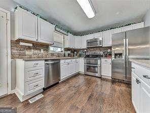 kitchen with decorative backsplash, appliances with stainless steel finishes, white cabinetry, and dark wood-type flooring