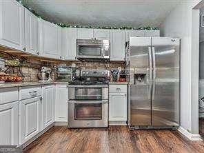 kitchen featuring tasteful backsplash, white cabinets, dark hardwood / wood-style floors, and appliances with stainless steel finishes