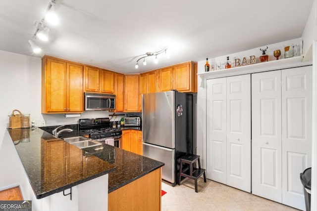 kitchen with kitchen peninsula, rail lighting, stainless steel appliances, sink, and dark stone countertops