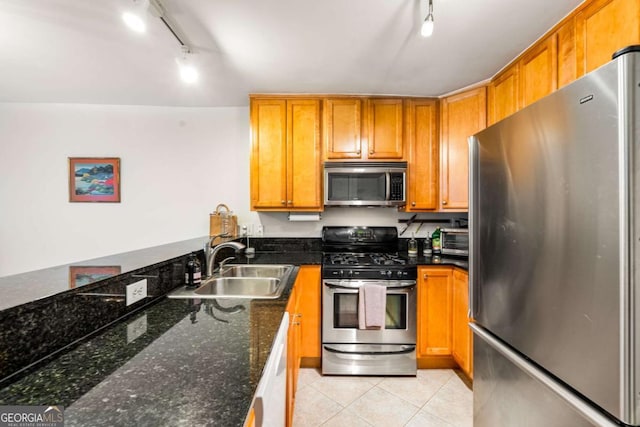 kitchen featuring rail lighting, sink, dark stone countertops, light tile patterned flooring, and stainless steel appliances