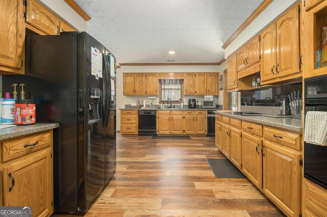 kitchen featuring a sink, wood-type flooring, black appliances, brown cabinetry, and a textured ceiling