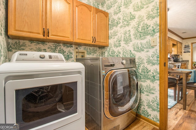 clothes washing area with cabinets, crown molding, light wood-type flooring, and washer and clothes dryer