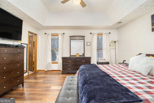 bedroom featuring a tray ceiling, dark hardwood / wood-style floors, and ceiling fan