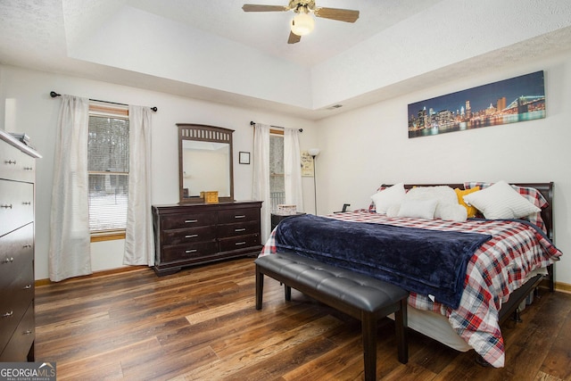 bedroom with dark wood-type flooring, ceiling fan, and a tray ceiling