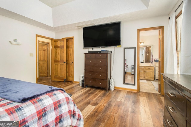 bedroom with hardwood / wood-style flooring, ensuite bath, and a tray ceiling