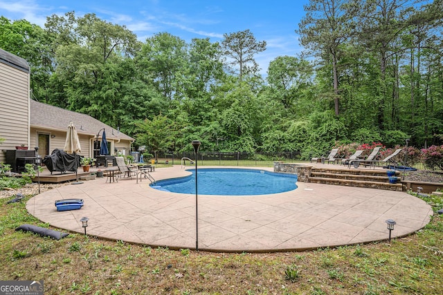 pool with a patio area, fence, and a deck