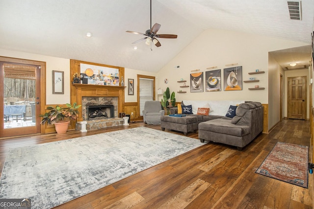 living room with dark wood-type flooring, ceiling fan, lofted ceiling, and a stone fireplace