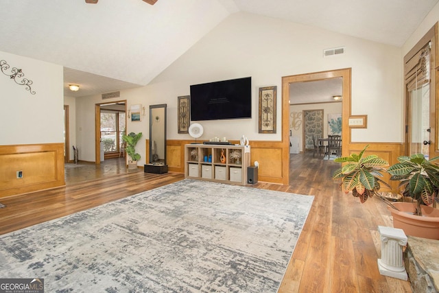 living room featuring hardwood / wood-style flooring, ceiling fan, wooden walls, and high vaulted ceiling