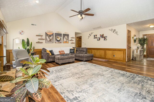 living room with a wainscoted wall, vaulted ceiling, wood finished floors, visible vents, and ceiling fan