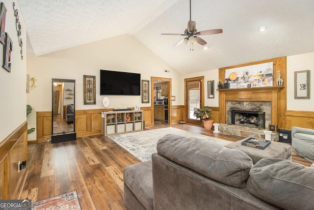 living room featuring vaulted ceiling, a textured ceiling, hardwood / wood-style flooring, ceiling fan, and a fireplace