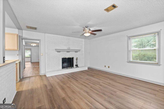 unfurnished living room featuring a fireplace, a healthy amount of sunlight, a textured ceiling, and light hardwood / wood-style flooring