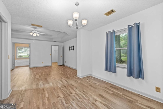 unfurnished living room featuring a textured ceiling, ceiling fan with notable chandelier, a tray ceiling, and light hardwood / wood-style flooring