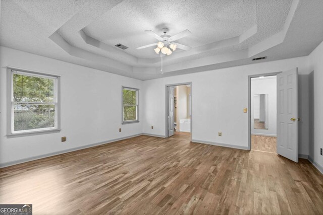 unfurnished bedroom with multiple windows, connected bathroom, a raised ceiling, and ceiling fan