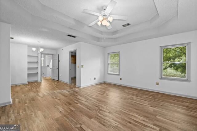 unfurnished living room featuring ceiling fan with notable chandelier, hardwood / wood-style flooring, a textured ceiling, a tray ceiling, and plenty of natural light