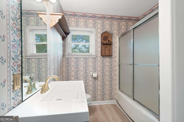 full bathroom with a textured ceiling, sink, shower / bath combination with glass door, hardwood / wood-style flooring, and toilet