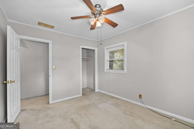 unfurnished bedroom featuring ceiling fan, light carpet, a textured ceiling, and ornamental molding