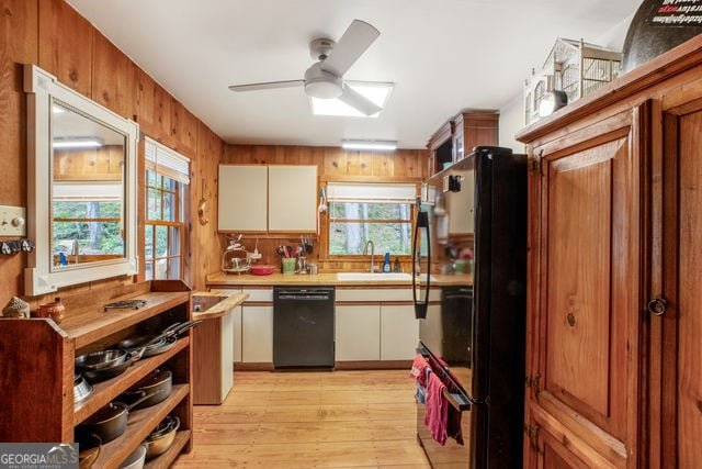 kitchen with ceiling fan, sink, wood walls, white cabinets, and black appliances