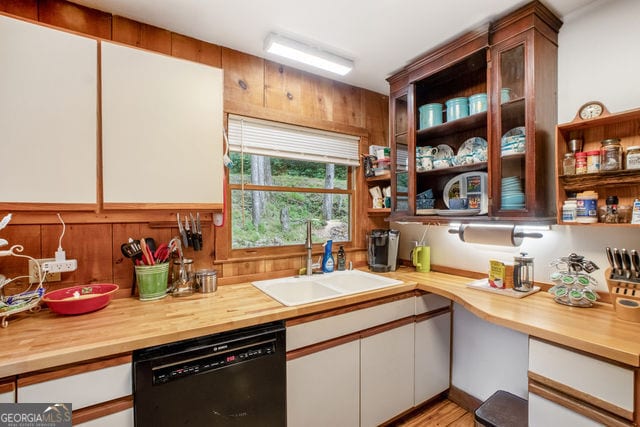 kitchen featuring white cabinets, dishwasher, wood walls, and sink