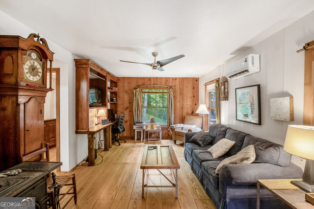 living room with a wall mounted air conditioner, ceiling fan, light wood-type flooring, and wooden walls