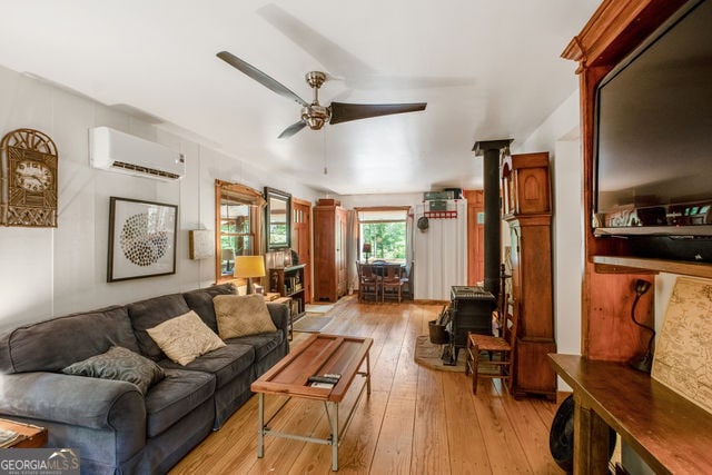 living room with a wall mounted air conditioner, ceiling fan, light wood-type flooring, and a wood stove