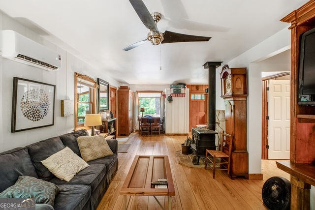 living room with ceiling fan, light hardwood / wood-style floors, a wood stove, and an AC wall unit