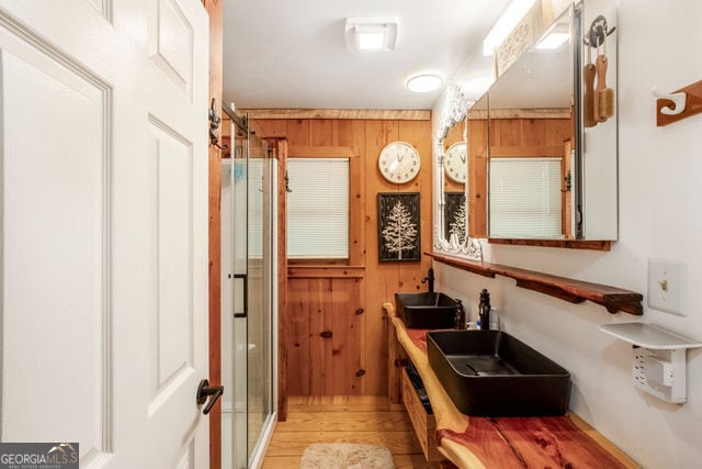 bathroom with hardwood / wood-style flooring, wood walls, and double sink