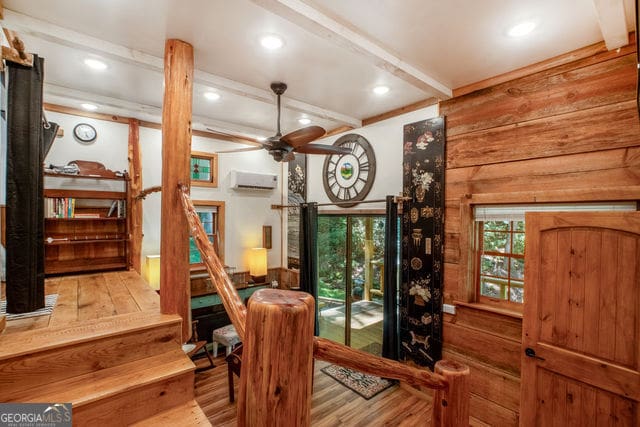 dining room featuring beamed ceiling, hardwood / wood-style floors, a wall mounted AC, and ceiling fan