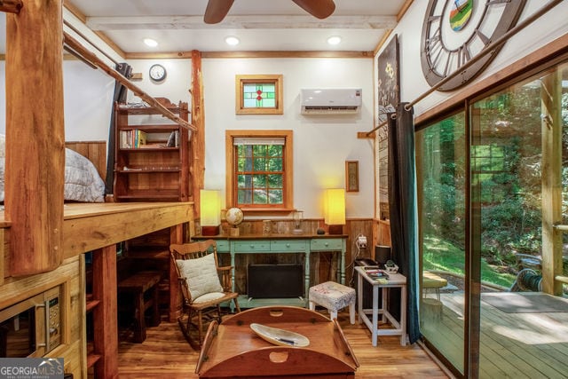 living area with a wall unit AC, wood walls, ceiling fan, and light wood-type flooring