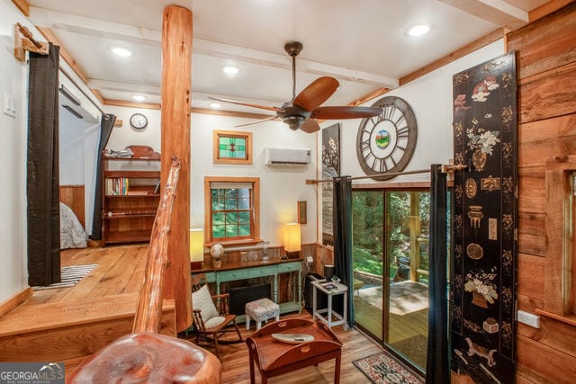 sitting room with hardwood / wood-style floors, wooden walls, ceiling fan, a wall mounted AC, and beam ceiling