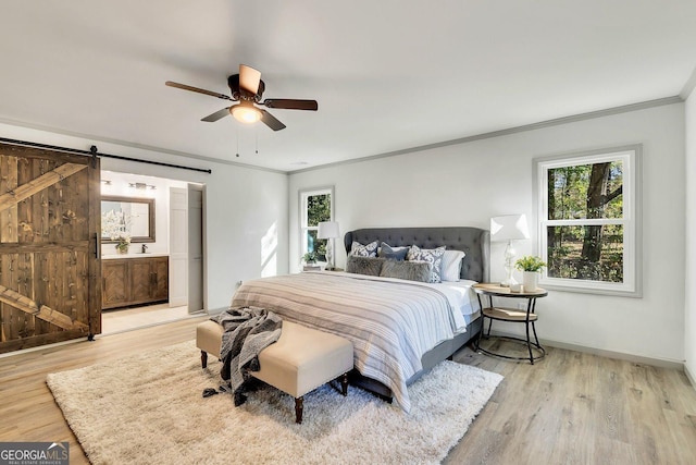 bedroom featuring a barn door, light hardwood / wood-style flooring, ceiling fan, and crown molding