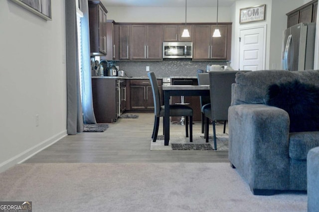 kitchen with pendant lighting, light hardwood / wood-style flooring, appliances with stainless steel finishes, backsplash, and dark brown cabinetry